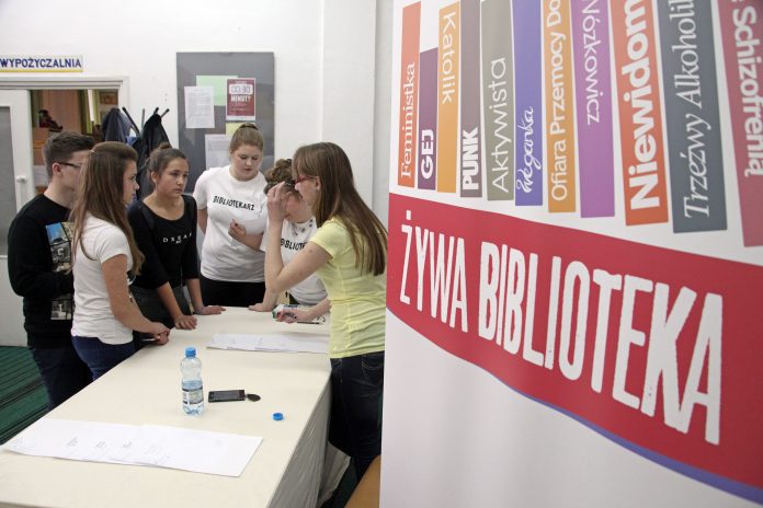 zywa-ksiazka_1 widok na Biblotekę, młodziez sojaca przy stole, czekajaca na zapisy do akcji Zywa Biblioteka