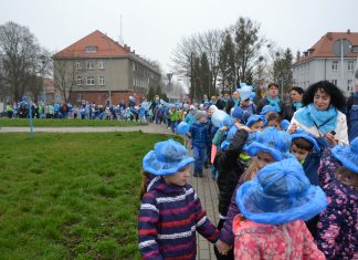 Zdjęcie przedstawia dzieci z niebieskim kapelusikami maszerujące chodnikiem, w oddali widać, że pochód jest długi, zakręca i kończy się poza kadrem.