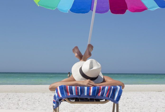 plaża , kobieta na leżaku pod parasolem z kapeluszem na głowie