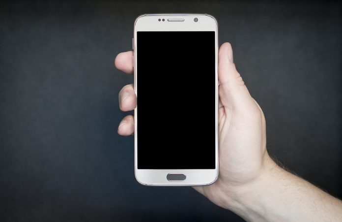 na szarym tele ręka trzymająca biały smartphone