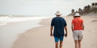 Zdjęcie przedstawia dwóch seniorów kobietę i mężczyznę idących brzegiem plaży.