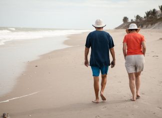 Zdjęcie przedstawia dwóch seniorów kobietę i mężczyznę idących brzegiem plaży.