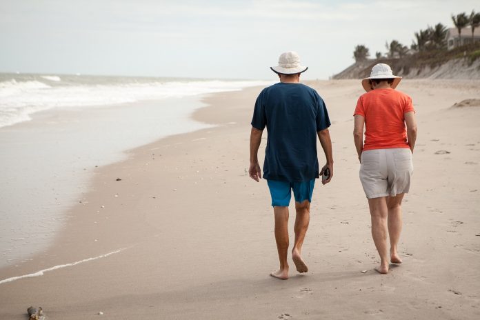 Zdjęcie przedstawia dwóch seniorów kobietę i mężczyznę idących brzegiem plaży.